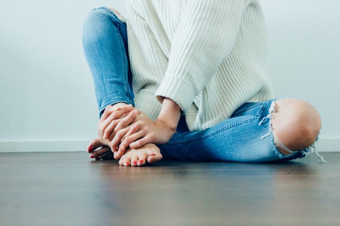 Kvinde sidder på gulvet i jeans og sweater