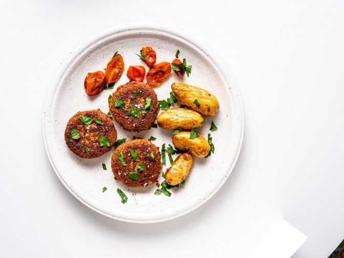Veganske burgere med kartofler og tomater på tallerkenen.