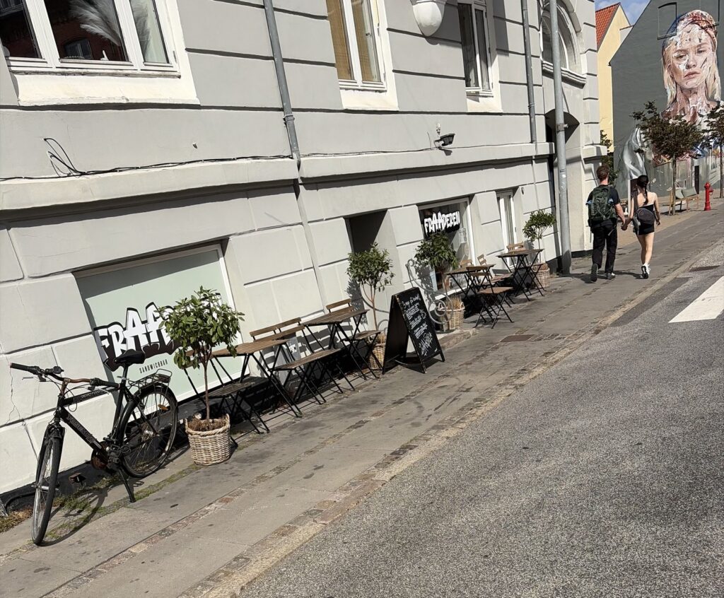 Facaden på FrAAderen sandwichbar i Danmarksgade i Aalborg med udendørs borde, menuskilt på fortovet og cykel foran vinduet