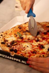 Pizza med blandet topping skæres ud